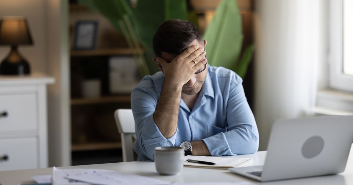 A man is sitting in front of his laptop with his head in his hands as he experiences startup burnout.